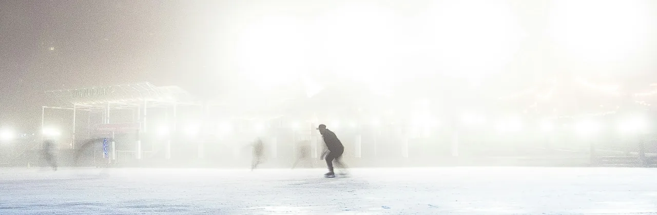 A skater alone on a floodlit outdoor rink in fog